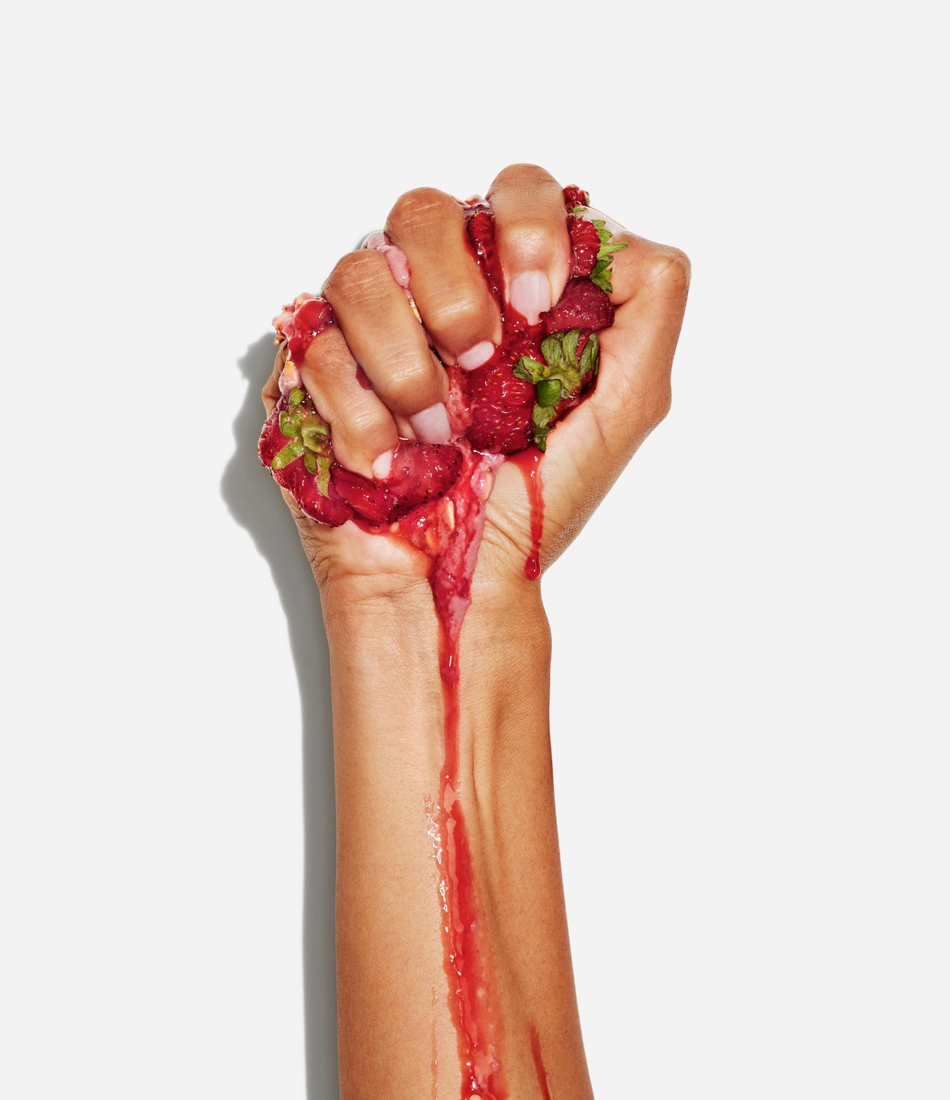 Close up of hand squeezing strawberries with juice dripping down arm